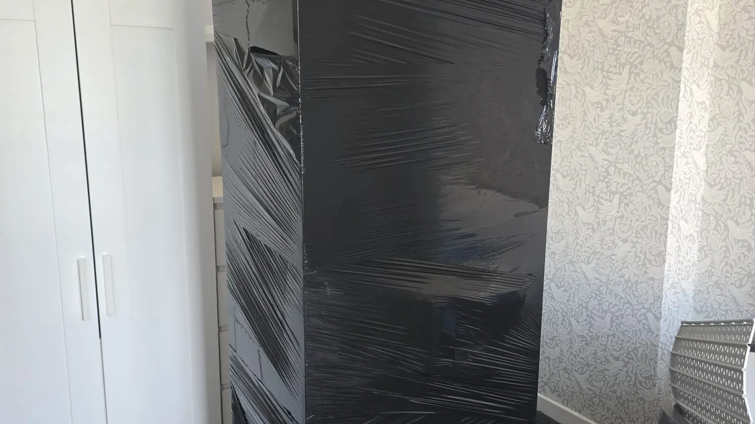 Wardrobe shrink-wrapped for transit standing in a customer bedroom